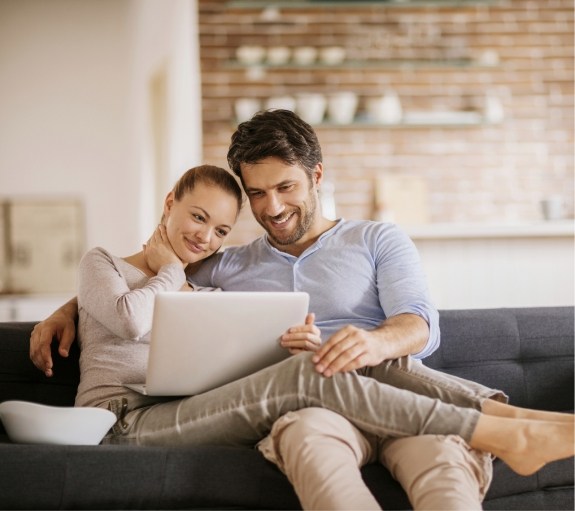 Man and woman sitting on couch looking at laptop