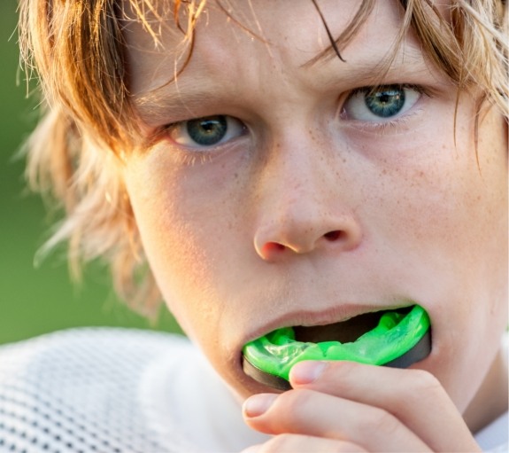 Young boy placing green athletic mouthguard over his teeth