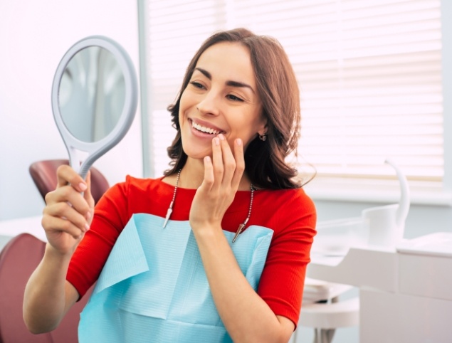 Woman admiring her smile in mirror after cosmetic dentistry in Topsham