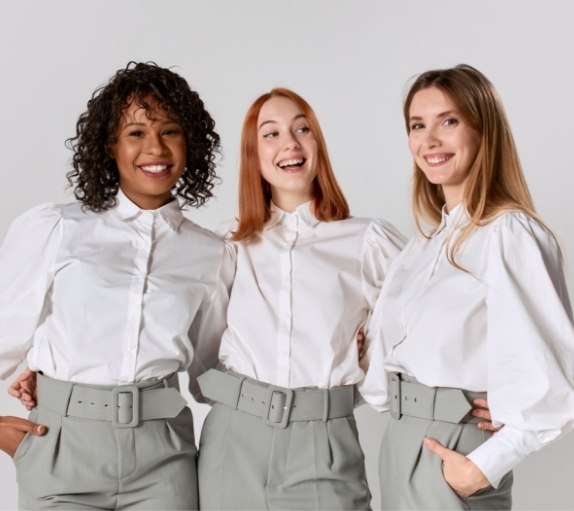 Three smiling dental team members in matching white shirts and khaki pants