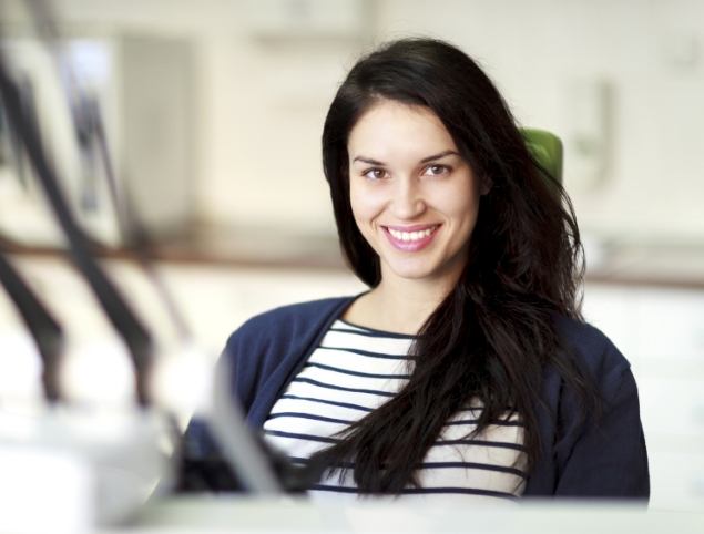 Smiling Topsham dental team member sitting at desk