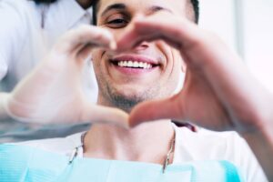 Man and dentist making a heart with their hands that frames his smile